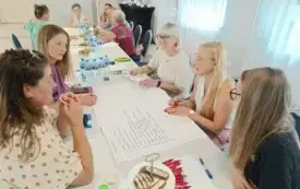 zdjecie przedstawiające osoby siedzące na krzesłach przy stole i rozmawiające