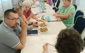 zdjecie przedstawiające osoby siedzące na krzesłach przy stole i rozmawiające